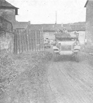 Half-track moves through opening in log road block left by Nazis in German village.
