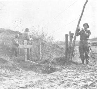 Yank soldiers string wire past the burial site of a German soldier.